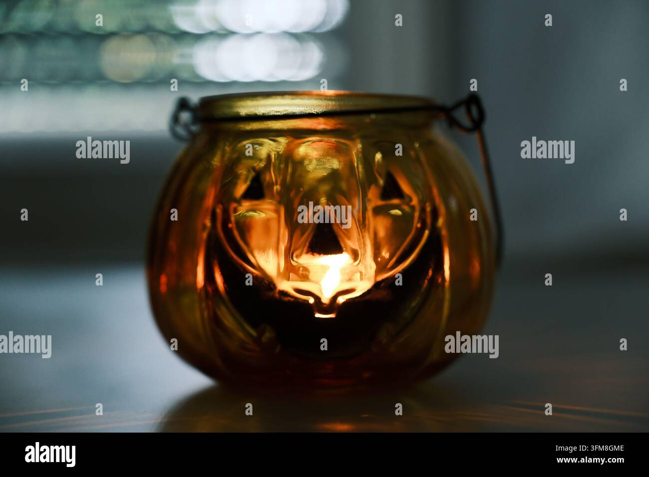 Lanterne en forme de citrouille en verre avec une bougie allumée à l'intérieur, créant une atmosphère automnale et Halloween chaleureuse. Banque D'Images