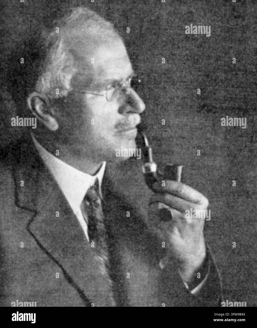 Une photographie de Carl Gustav Jung (1875–1961), le psychiatre et psychanalyste suisse qui a fondé la psychologie analytique. Après sa collaboration précoce avec Sigmund Freud, Jung a développé ses propres théories influentes concernant la psyché humaine, y compris les concepts de l'inconscient collectif, de la synchronicité et des figures archétypales. Il est représenté ici de profil, portant un costume et des lunettes sans monture tout en tenant une pipe à tabac. C. 1935. Banque D'Images