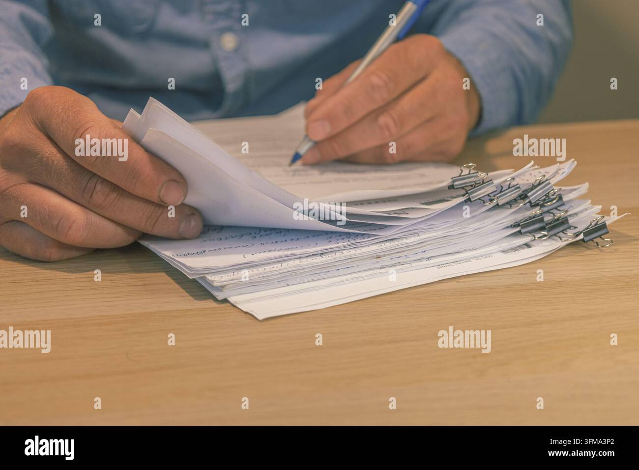 Mains remplissant et signant des documents contractuels d'entreprise organisés avec des pinces à reliure noires sur un bureau en bois. Approbation d'accord commercial, documents fiscaux Banque D'Images