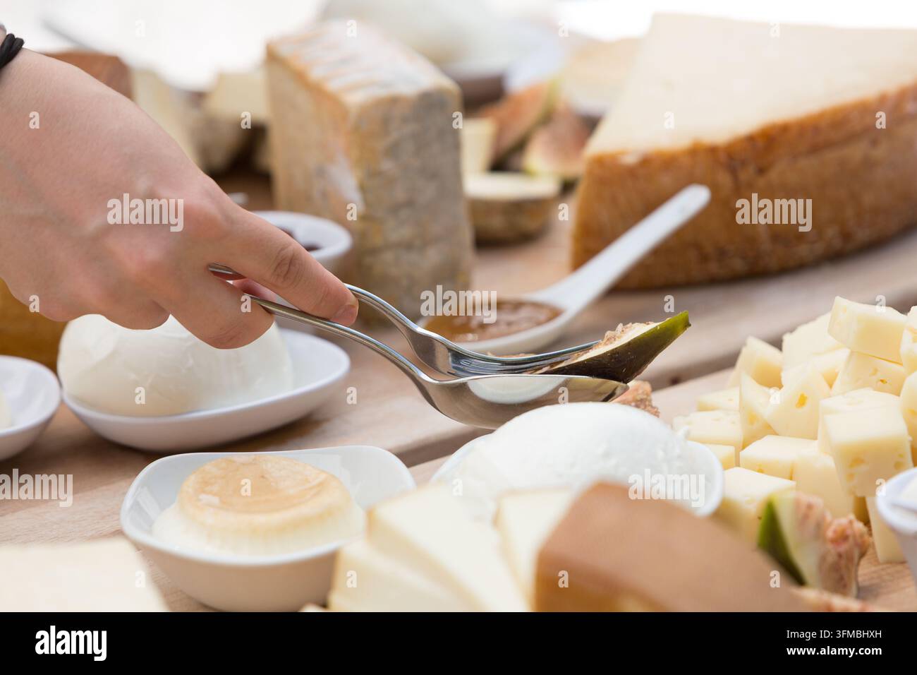 Main utilisant des pinces pour servir une figue d'un tableau en bois rustique avec divers fromages Banque D'Images