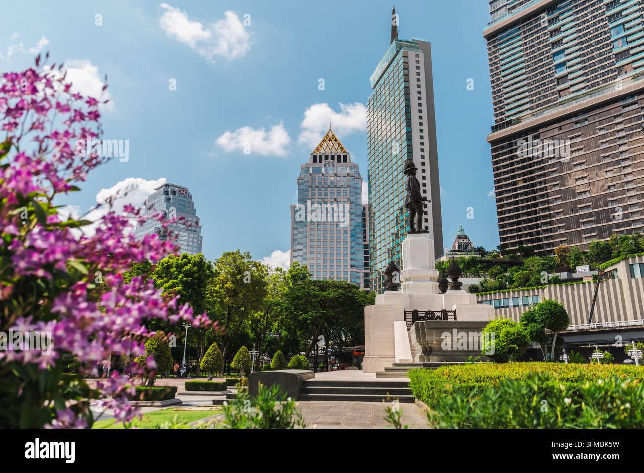 Bangkok, Thaïlande, 3 mai 2026 : La ligne d'horizon et le monument de Bangkok s'élèvent derrière un jardin paysagé avec des fleurs violettes sous un ciel bleu éclatant. Banque D'Images