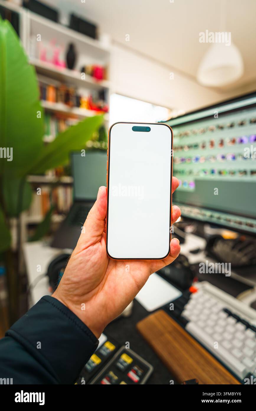Main tenant un écran de smartphone en guise de modèle sur un fond de studio de photographie avec synchronisation cloud. Gros plan d'un créateur de contenu tenant un téléphone mobile avec un écran clair Banque D'Images