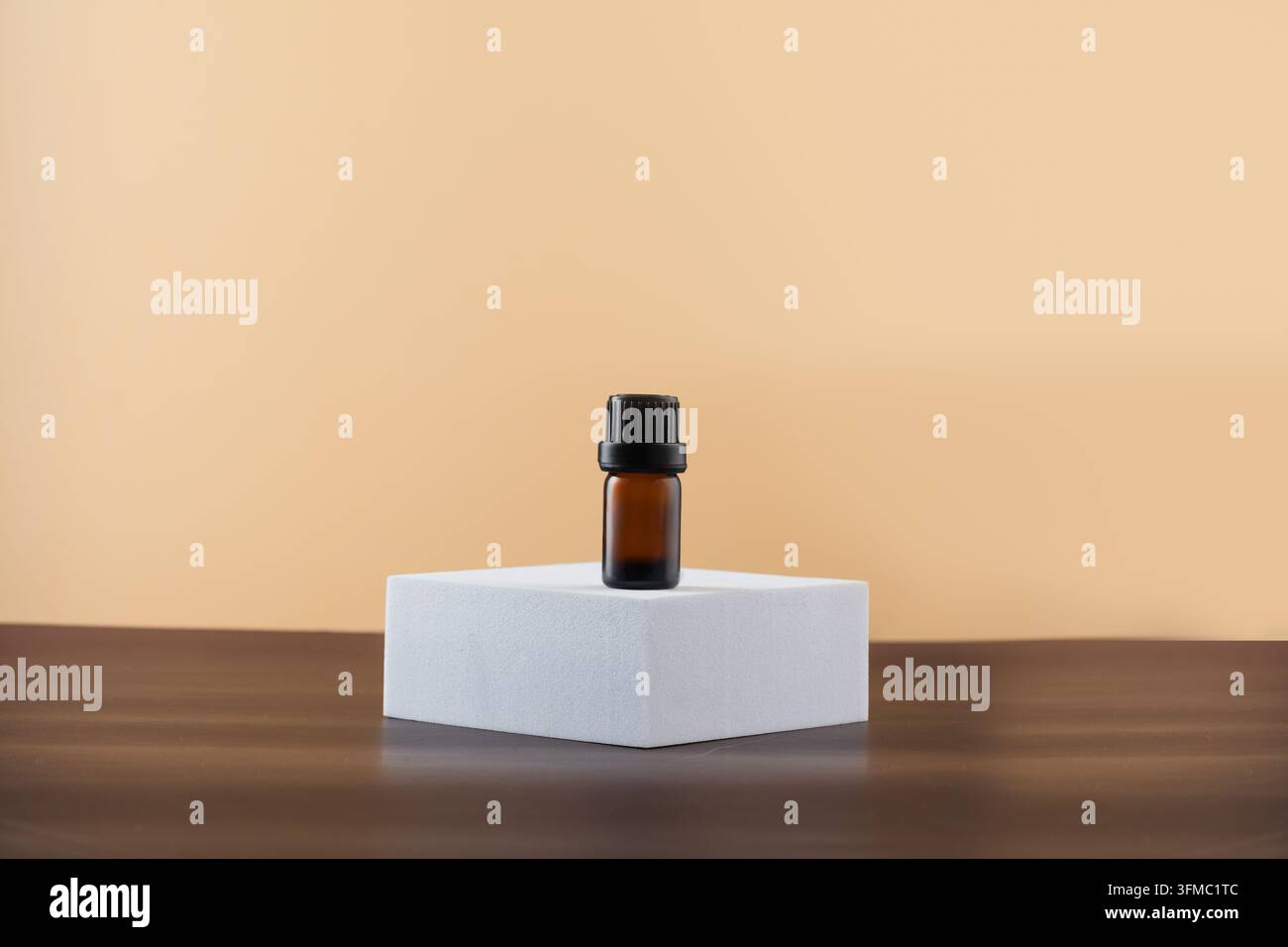 Petite bouteille en verre ambré de 5 ml pour huile essentielle sur un podium hexagonal blanc, fond beige Banque D'Images