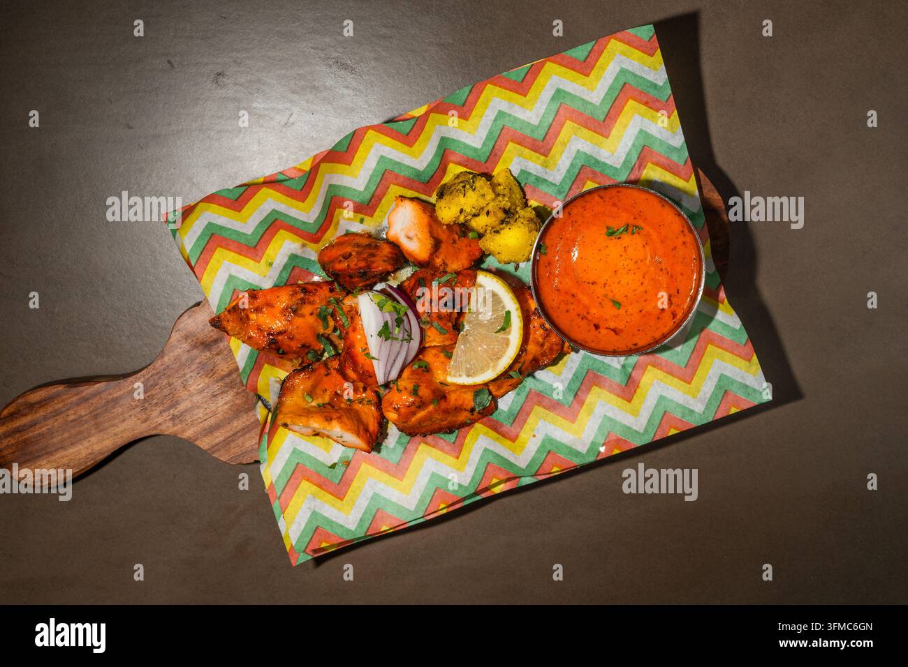 Poulet tandoori avec des quartiers de citron et une sauce de trempage sur une planche en bois, vue de dessus Banque D'Images