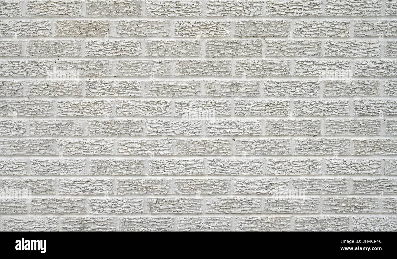 Mur de briques texturé peint en blanc avec des faces de briques rugueuses et irrégulières dans une composition horizontale, montrant un motif de liant décalé Banque D'Images