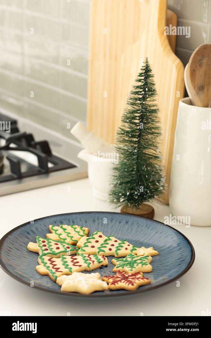 Une assiette bleue contenant des biscuits glacés en forme d'arbre de Noël et de flocon de neige sur le comptoir près de la cuisinière Banque D'Images