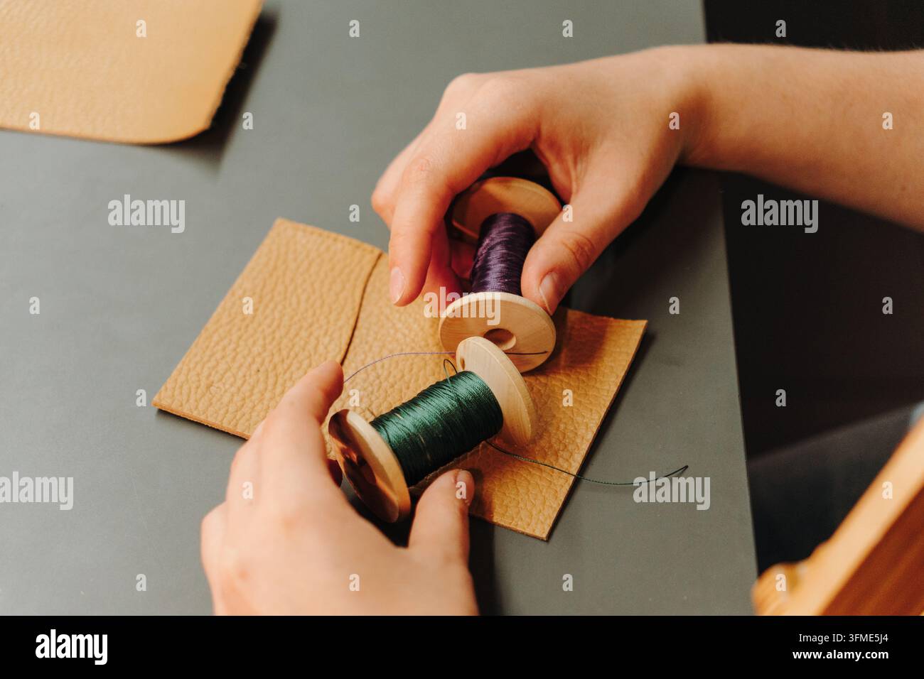Des mains comparent des bobines de fil vert et violet sur des pièces en cuir texturé. Concept de préparation pour le cuir, la couture à la main, le design et l'accessoire personnalisé Banque D'Images