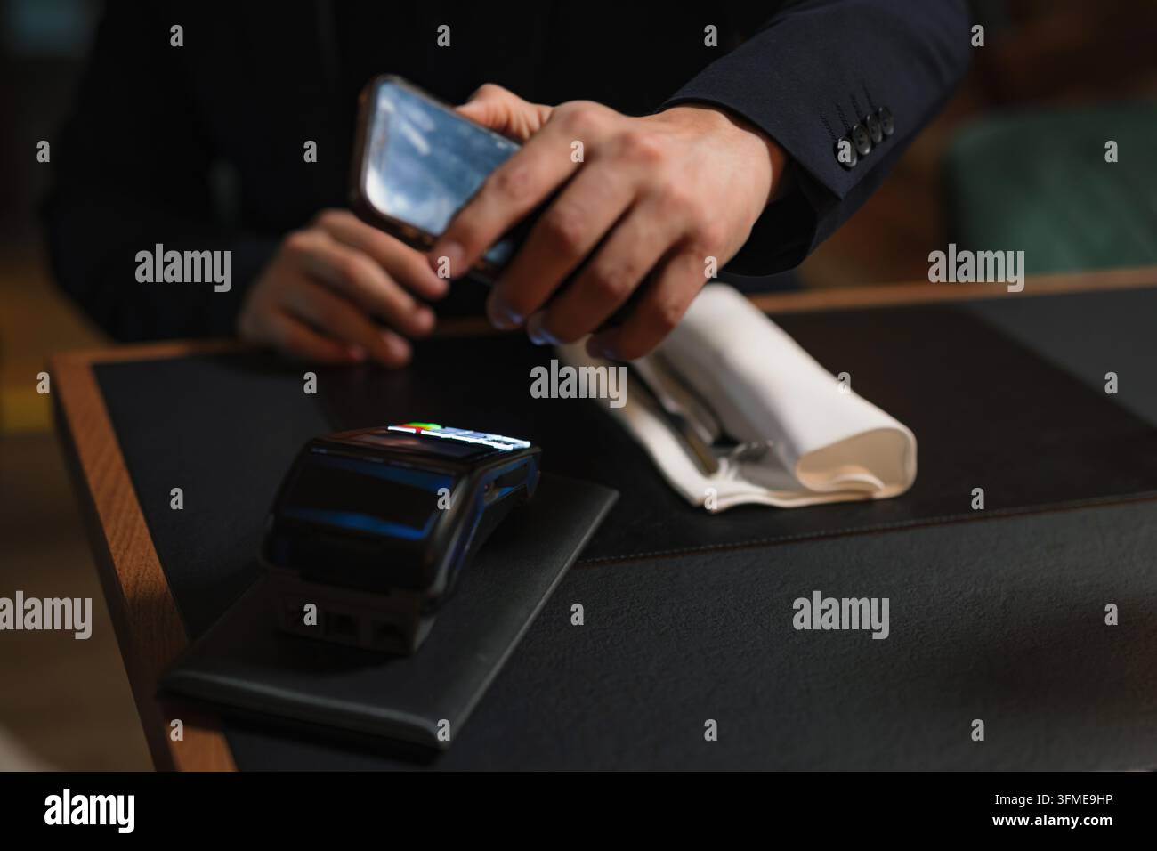 Homme effectuant une transaction de paiement mobile sur un terminal POS à une table de restaurant confortable pendant un dîner détendu, gros plan. Banque D'Images