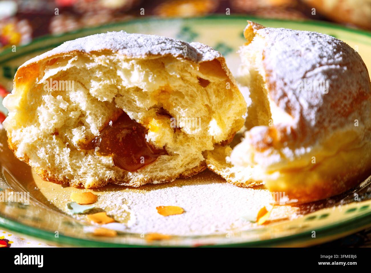 Beignets à la marmelade remplis de confiture d'abricot avec sucre en poudre, coupés en deux, assiette en céramique fondue blanche et verte, nappe à motifs, confettis Banque D'Images