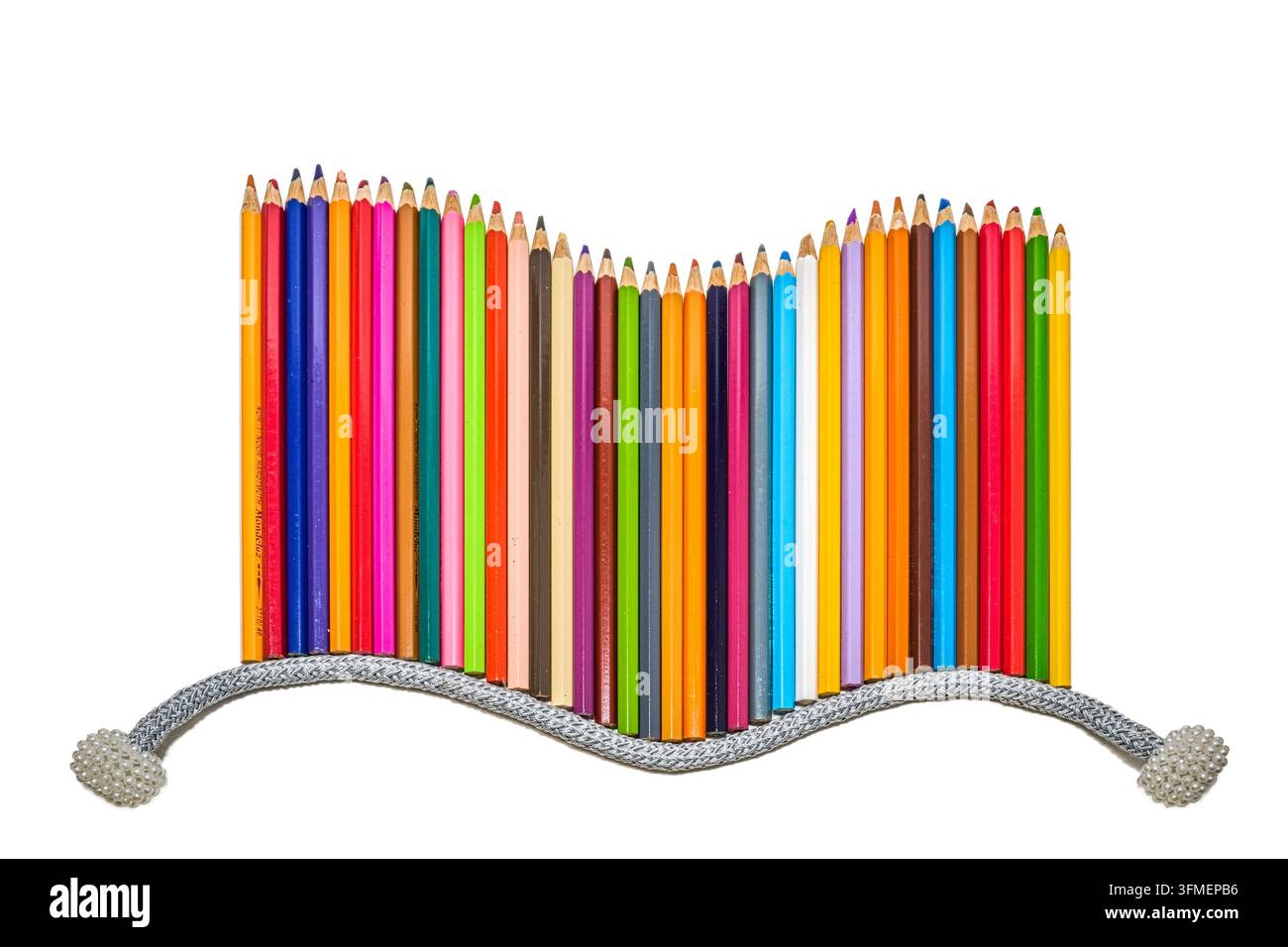 Range de crayons de couleur disposés en forme de vague avec un cordon décoratif en argent sur un fond blanc immaculé, design. Banque D'Images