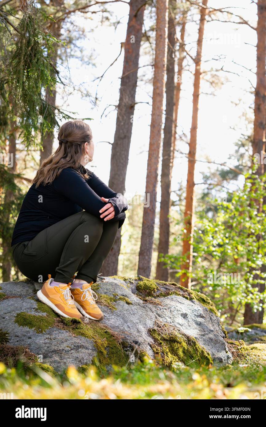 Une femme est assise détendue sur un rocher dans la forêt, profitant de la tranquillité Banque D'Images