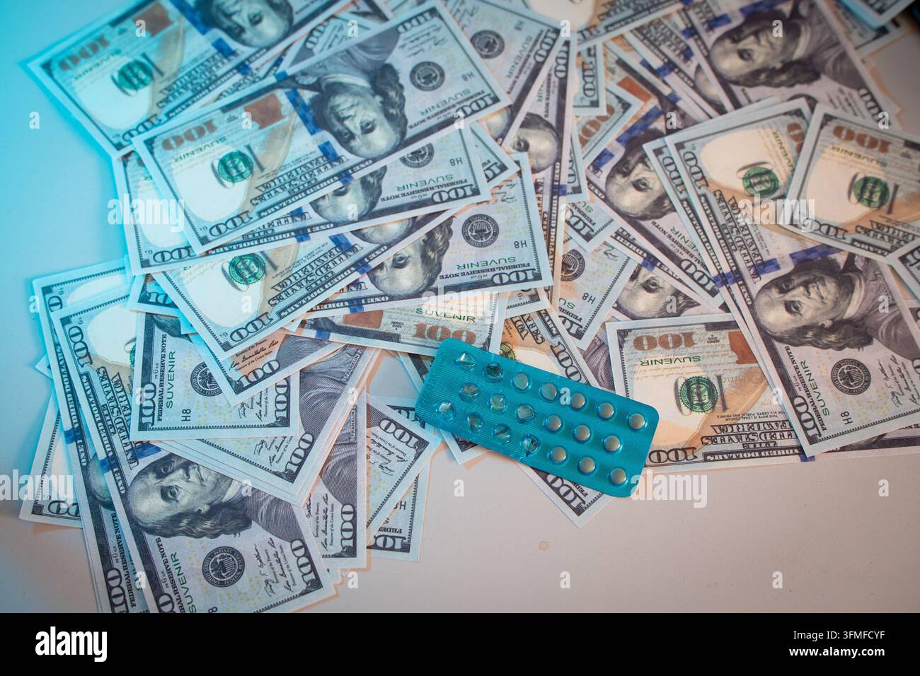 Une photographie en contre-plongée, vue du dessus, capturant un tas désordonné de nombreuses coupures de 100 dollars US en souvenir dispersées sur une surface plane, avec un bleu-vert Banque D'Images