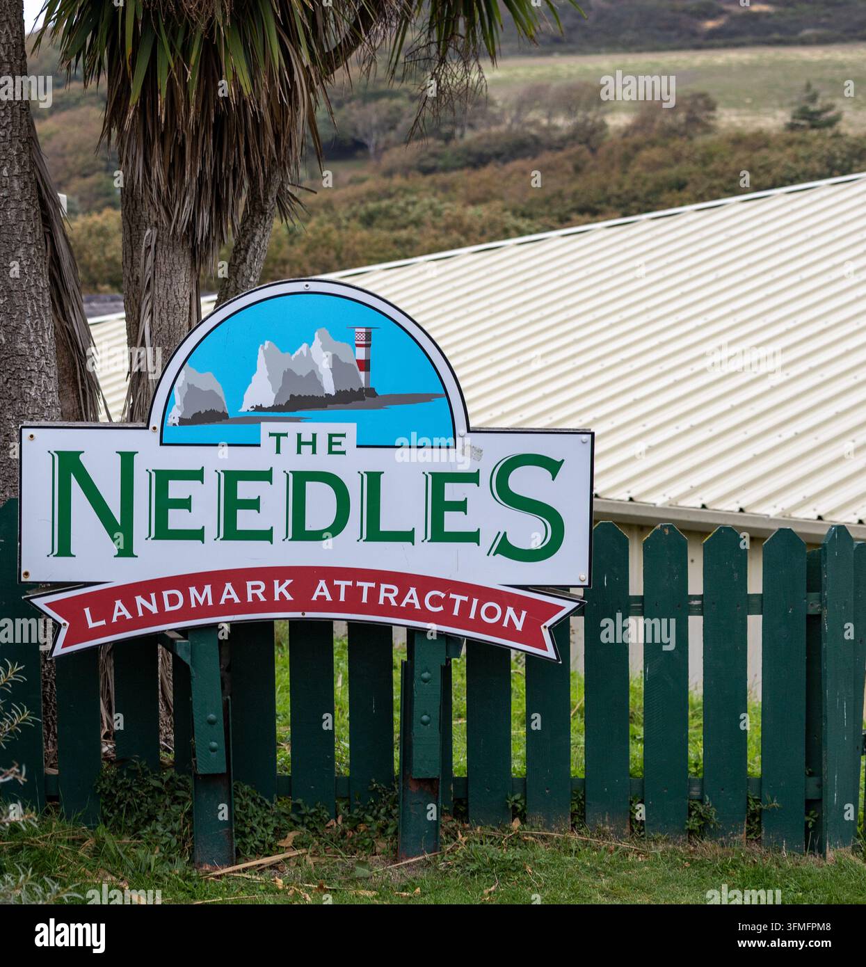 Panneau de l'attraction The Needles Landmark à Alum Bay sur l'Île de Wight, avec une illustration d'un phare à côté d'une clôture verte et d'arbres Banque D'Images