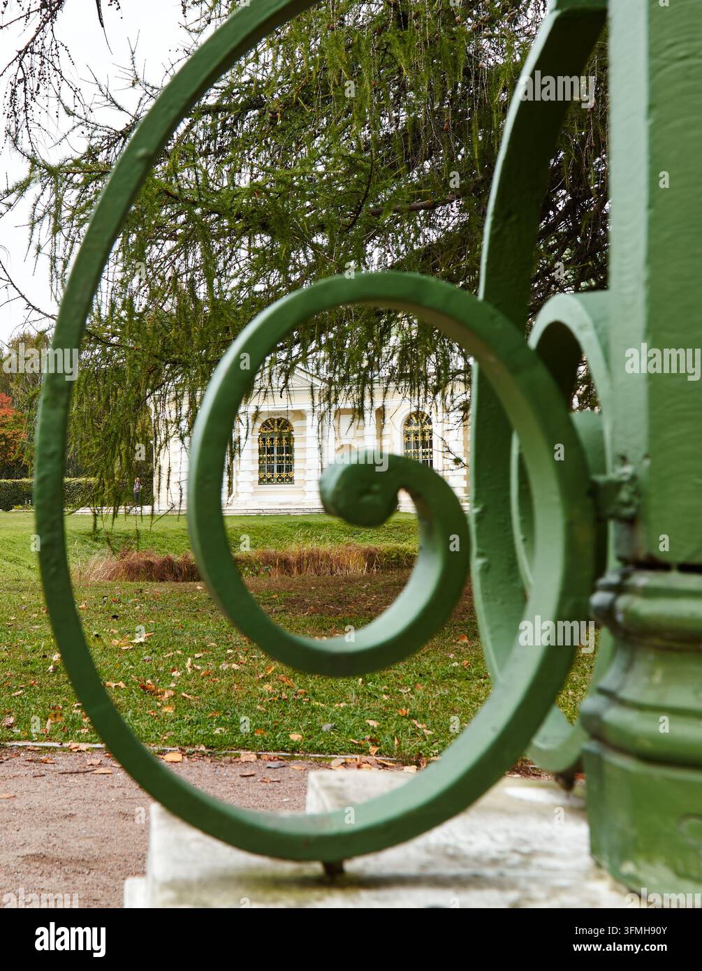 Moscou, Russie – 27 septembre 2026 : Une clôture en fer vert ornée encadre un pavillon historique blanc à travers une pelouse, avec des arbres d'automne et un chemin pavé dans le Banque D'Images
