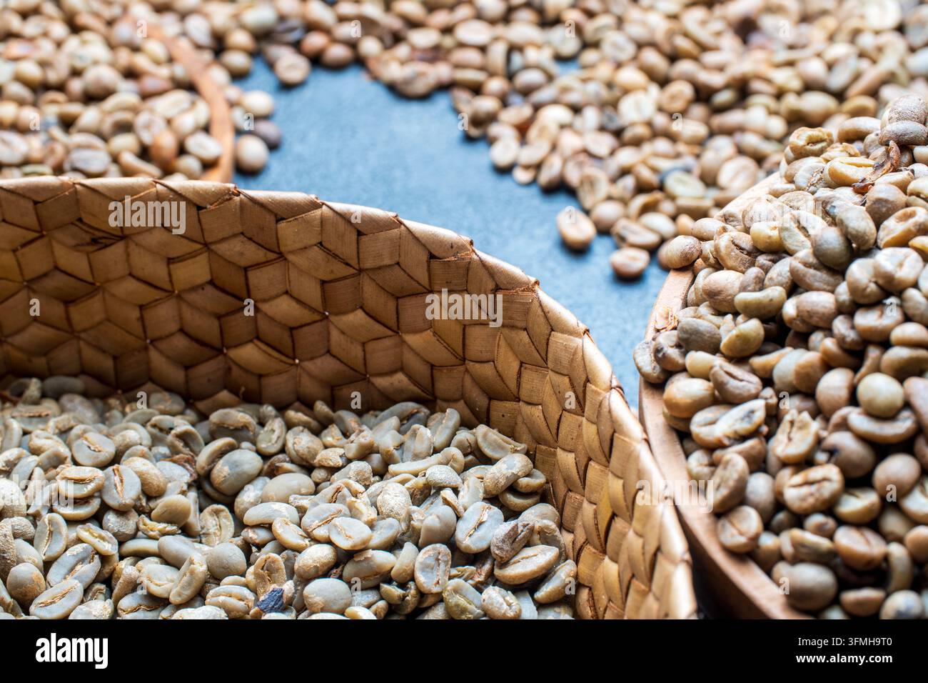 Grains de café verts non torréfiés remplis dans un panier tressé et un bol en bois sur une surface sombre avec mise au point sélective pour un thème agricole. Banque D'Images