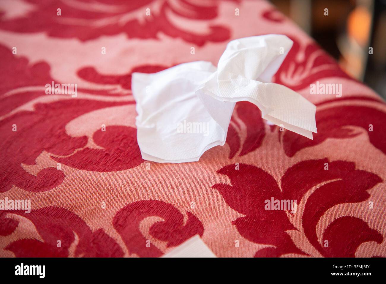 Mouchoir blanc froissé sur un tissu à motifs rouges avec un fond légèrement flou, éclairage intérieur chaud, détail de texture en gros plan, ménage quotidien calme Banque D'Images