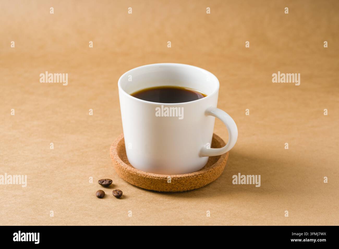 Tasse de café noire minimale avec des grains éparpillés sur une table chaude Banque D'Images