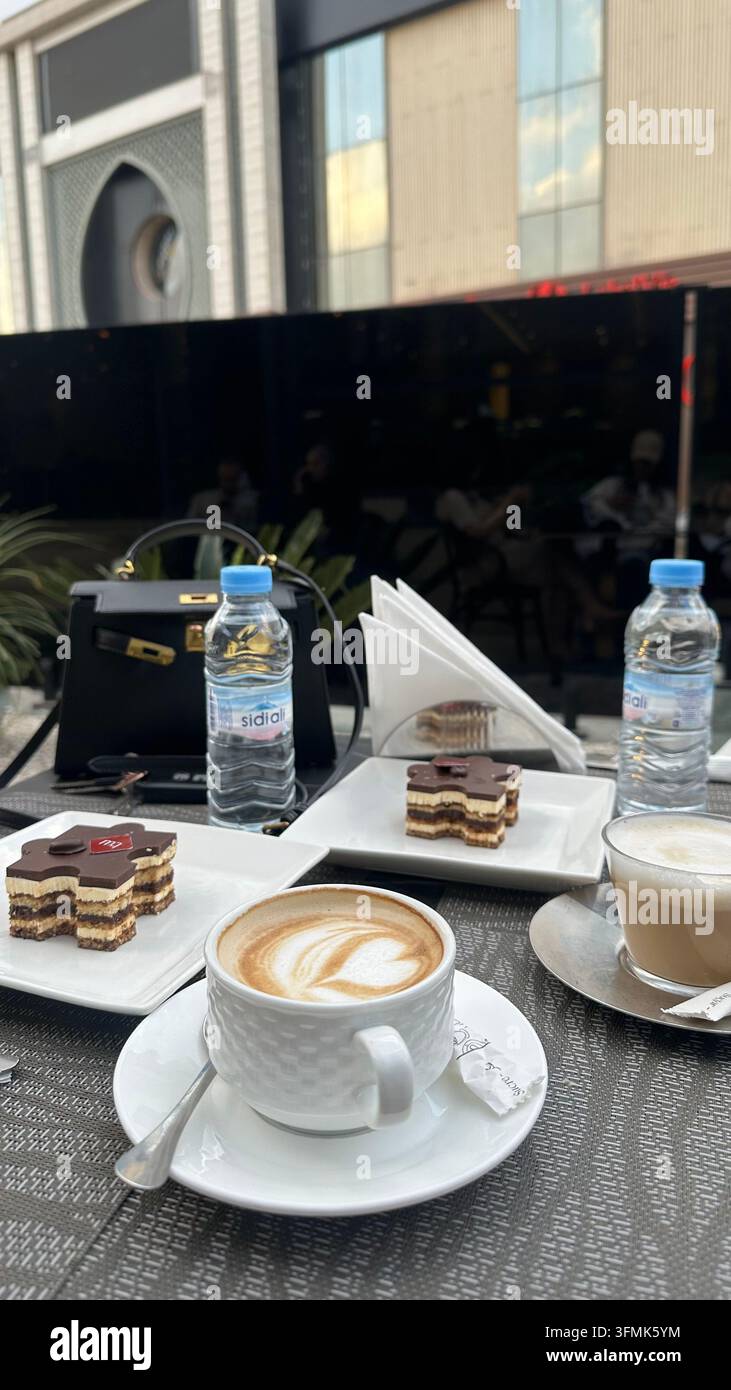 Cappuccino et pâtisseries servis avec de l'eau en bouteille sur une table de café dans un cadre urbain en plein air. - Image de stock capturée avec un smartphone