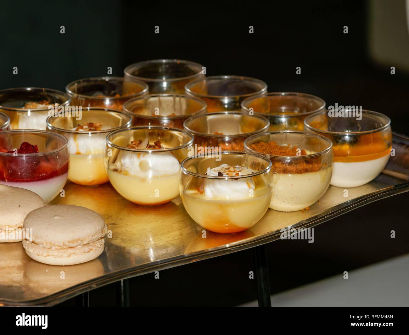 Diverses desserts individuels au custard et à la crème dans des verres sur un plateau avec des macarons Banque D'Images
