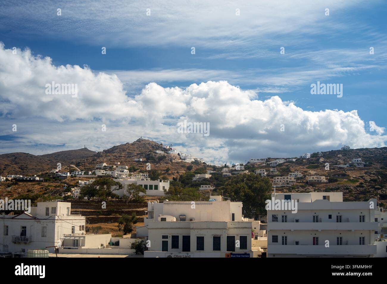 Vue du port d'Ios, Grèce, vers les maisons blanchies à la chaux de Chora dispersées sur les collines sèches des Cyclades sous un ciel dramatique. Banque D'Images