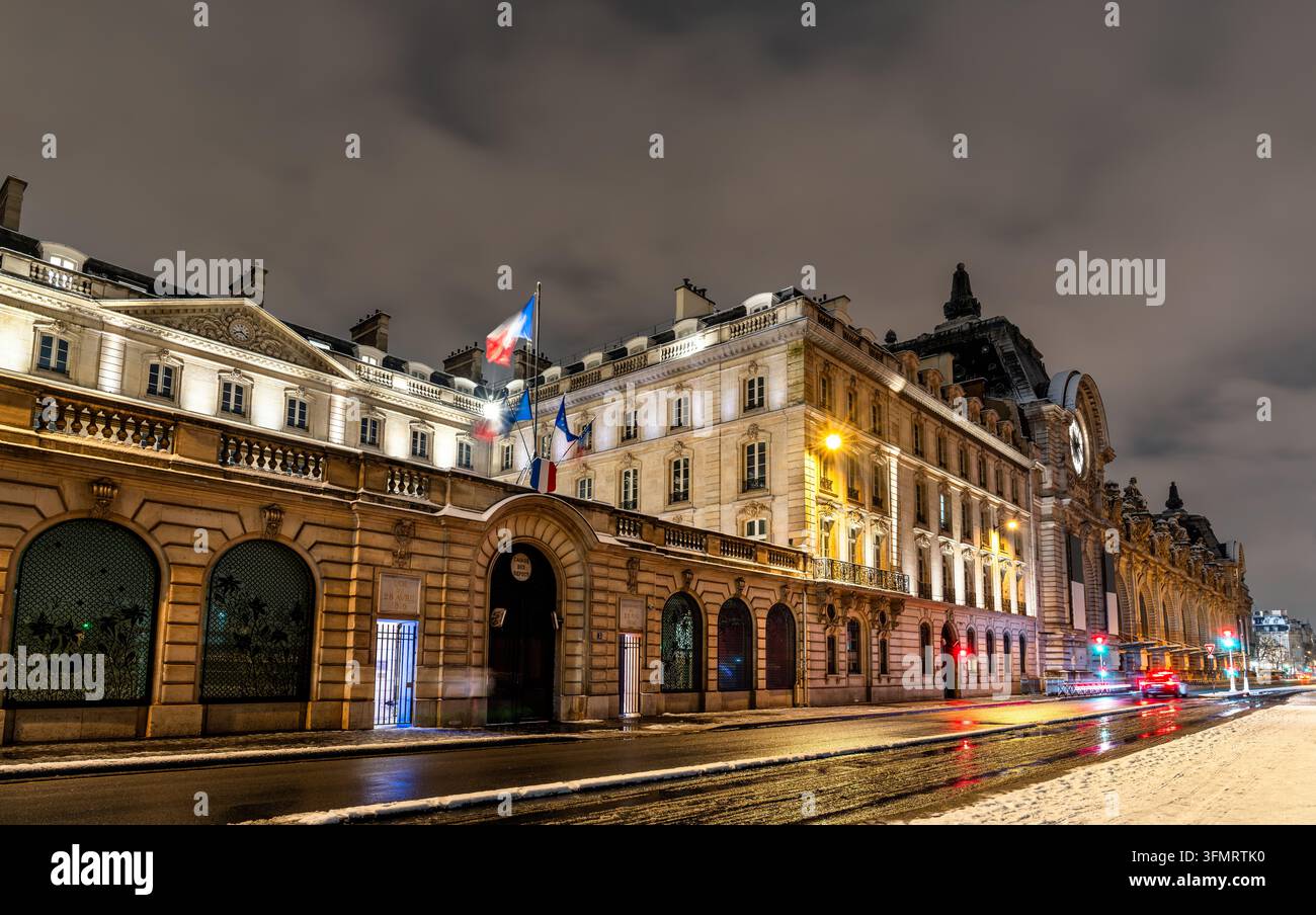 Vue nocturne illuminée du musée d'Orsay historique et des bâtiments du gouvernement français le long de la Seine sous un ciel hivernal enneigé à Paris, France. Banque D'Images