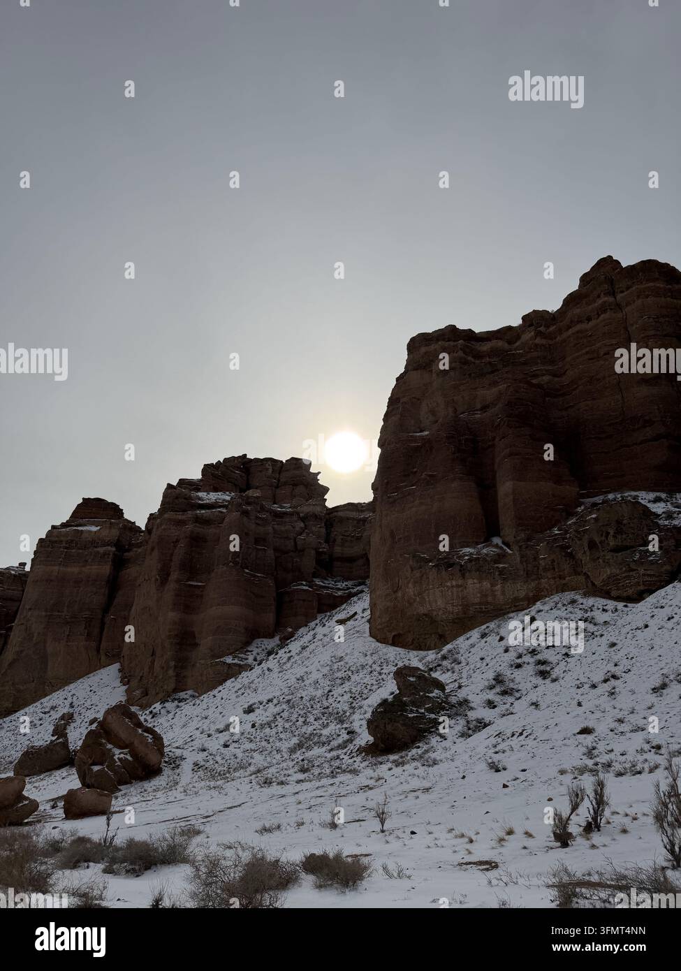 Le soleil d'hiver brille derrière des falaises monumentales de grès saupoudrées de neige dans le canyon de Charyn, région d'Almaty, Kazakhstan. - Image de stock capturée avec un smartphone