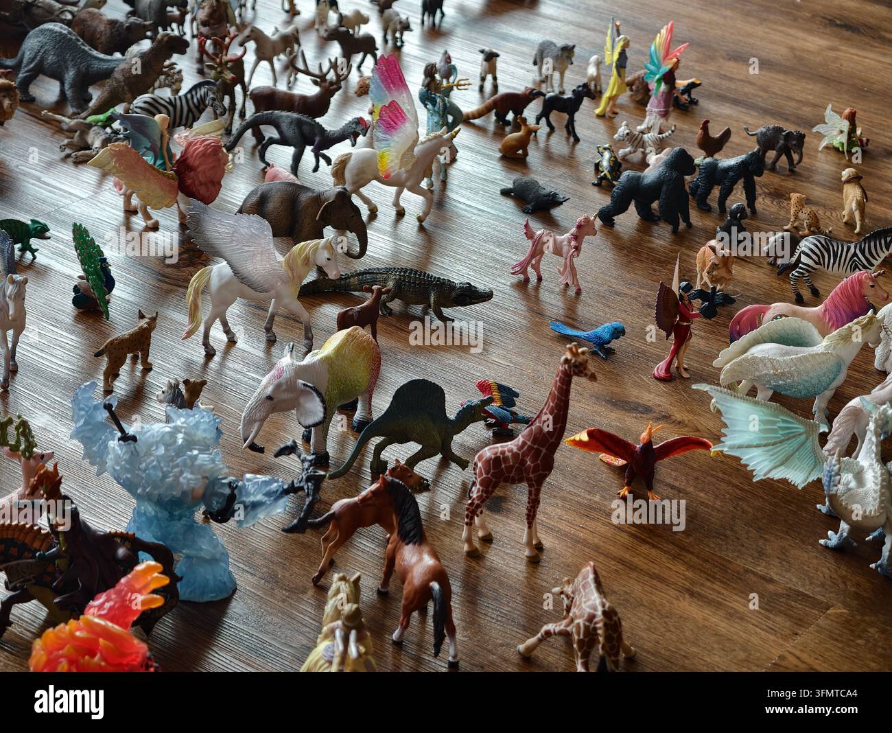 Petits animaux en plastique et figurines mythiques éparpillés sur un sol en bois poli, disposés dans des poses variées et vives. Cette scène colorée de jouets fonctionne Banque D'Images