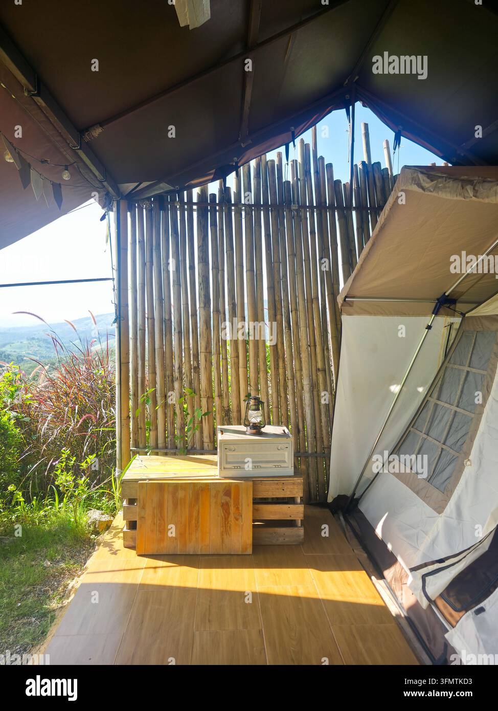 Un abri de glamping en plein air avec mur en bambou, tente en toile, sol en bois, vue sur les montagnes et poêle rustique baigné de soleil Banque D'Images