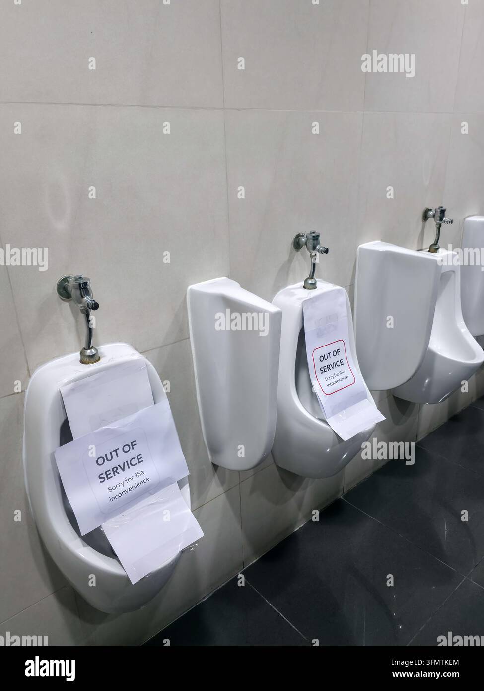Un urinoir de toilettes publiques avec panneaux « hors service », mettant l'accent sur l'hygiène, la maintenance et la fermeture temporaire de l'établissement dans un cadre de sanitaires carrelés Banque D'Images