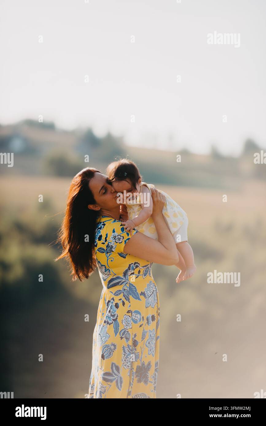Mère embrassant et tenant sa petite fille en plein air dans une campagne baignée de soleil, embrassant l'amour Banque D'Images