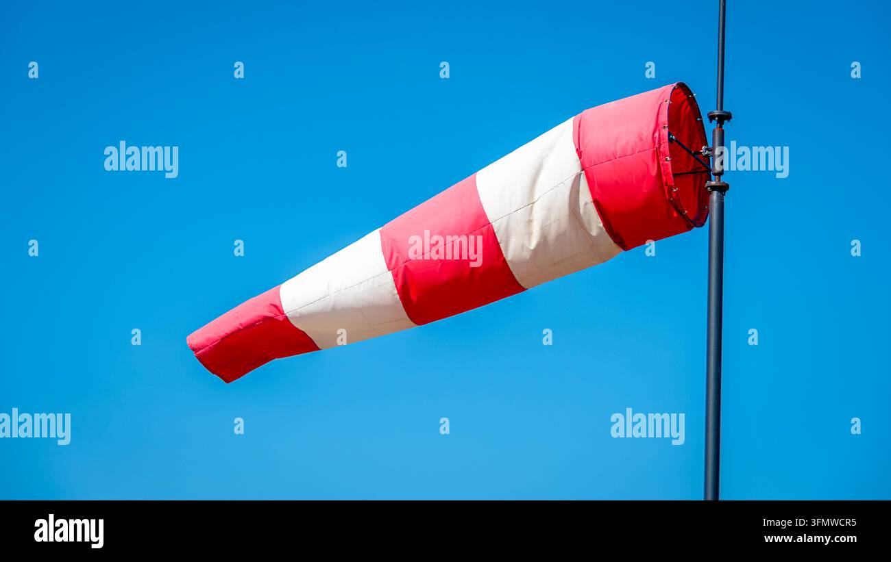 Mât de guidage rouge et blanc gonflé par le vent sur un fond de ciel bleu. Concepts de prévision météorologique, direction du vent et force du vent Banque D'Images