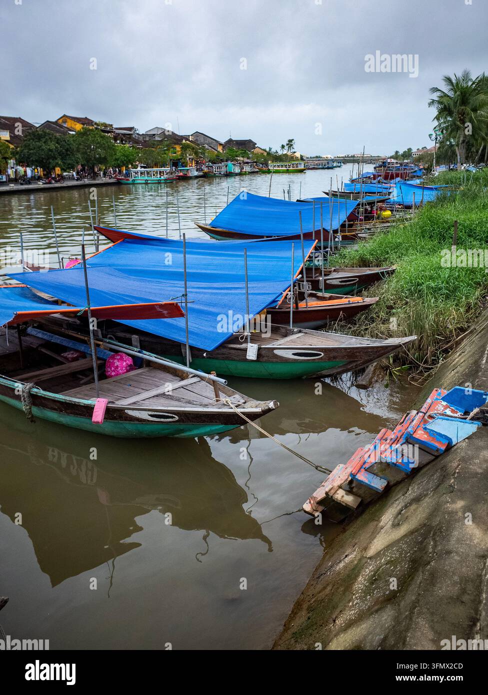 Bateaux fluviaux traditionnels en bois avec bâches bleues amarrés le long de la rivière Thu Bon à Hoi An Banque D'Images