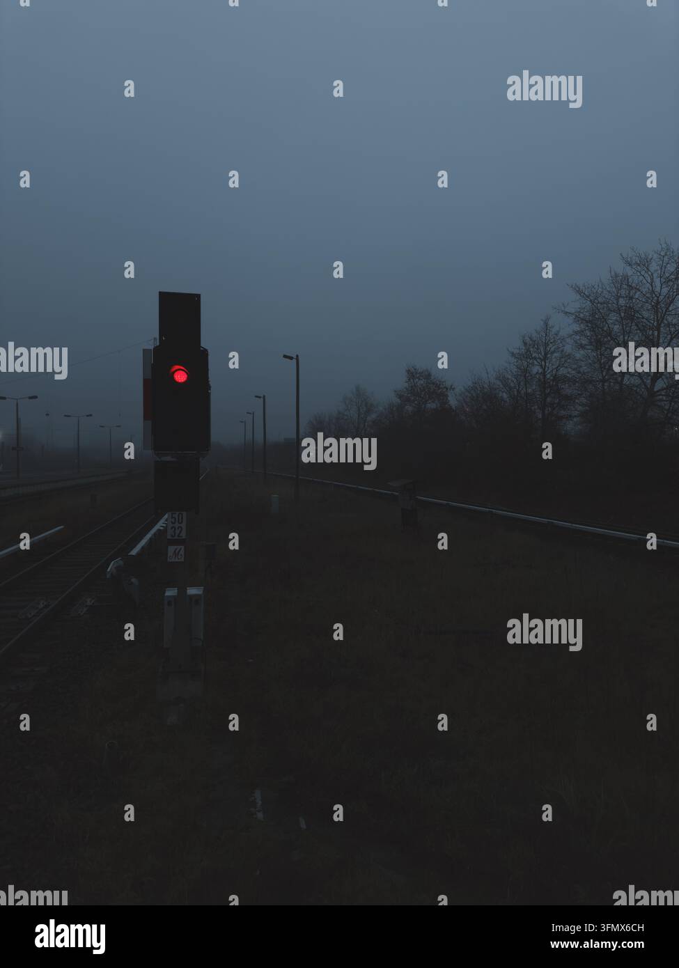 Une lumière rougeoyante sur un poteau de signalisation ferroviaire à côté des voies par une soirée froide, sombre et brumeuse, créant une atmosphère étrange et isolée. Banque D'Images