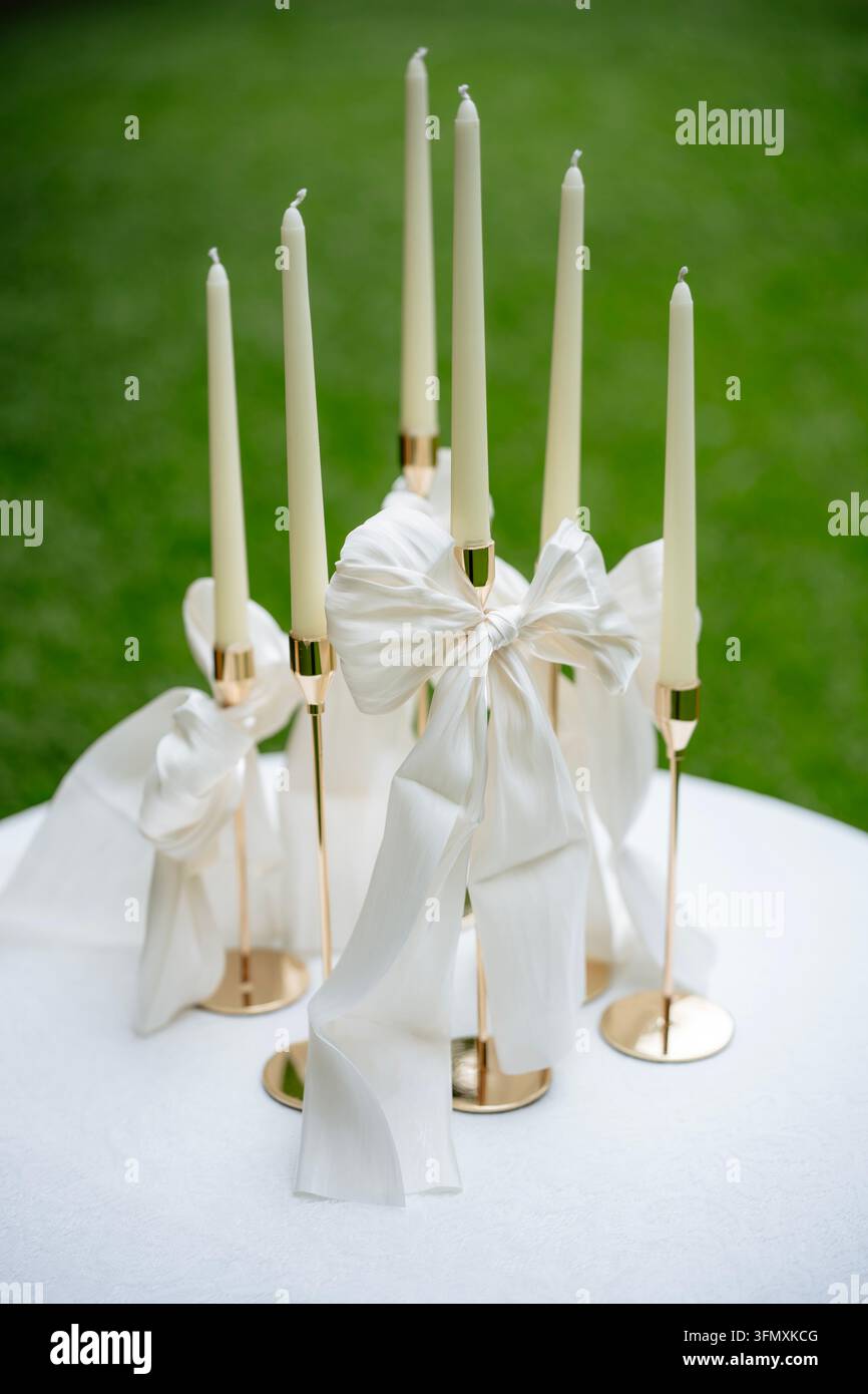 Chandelles coniques blanches élégantes dans des supports dorés décorés de nœuds en soie blanche Banque D'Images