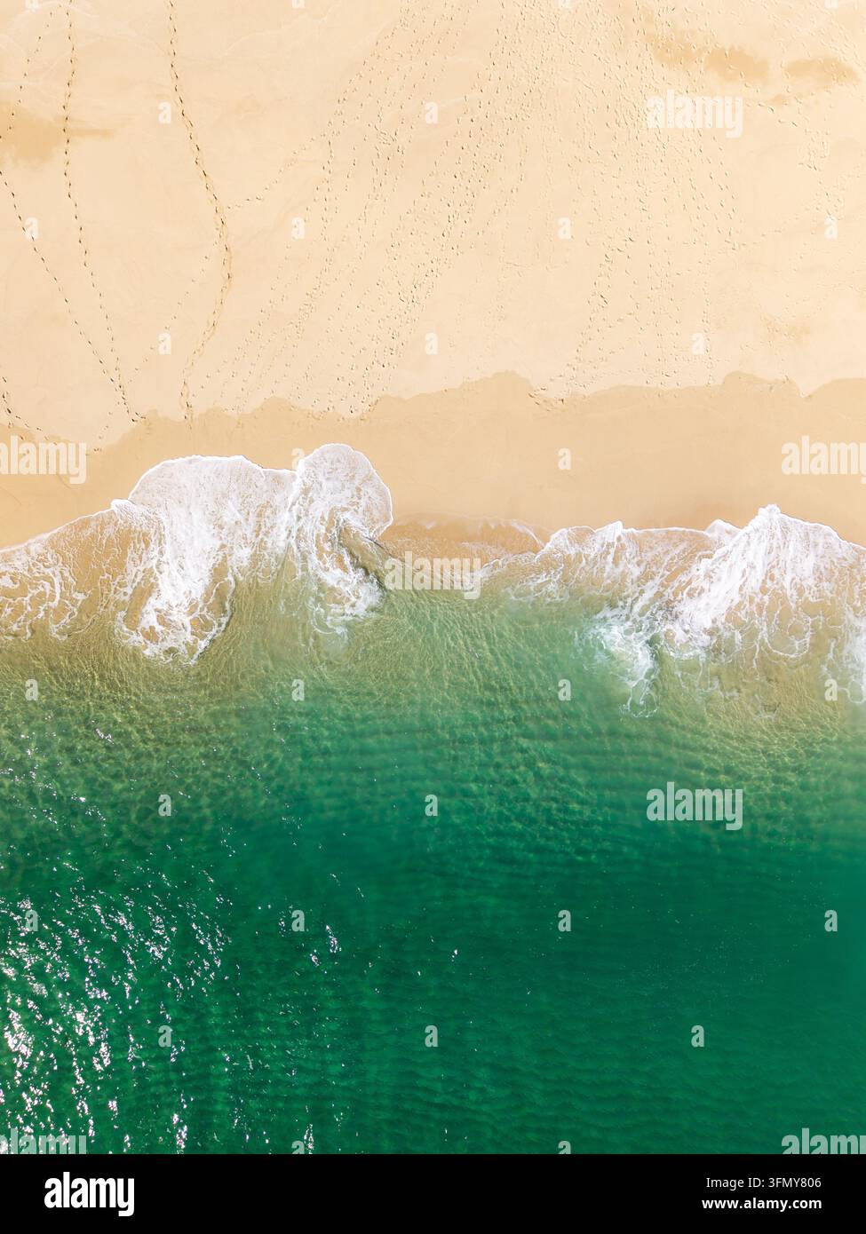 Paysage vertical aérien directement au-dessus des vagues blanches se brisant doucement sur un sable doux et doré parsemé d'empreintes de pas dans un paradis tropical ou un voyage Banque D'Images