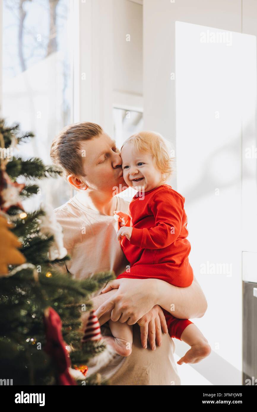 Père embrassant son fils bébé souriant près du sapin de Noël Banque D'Images