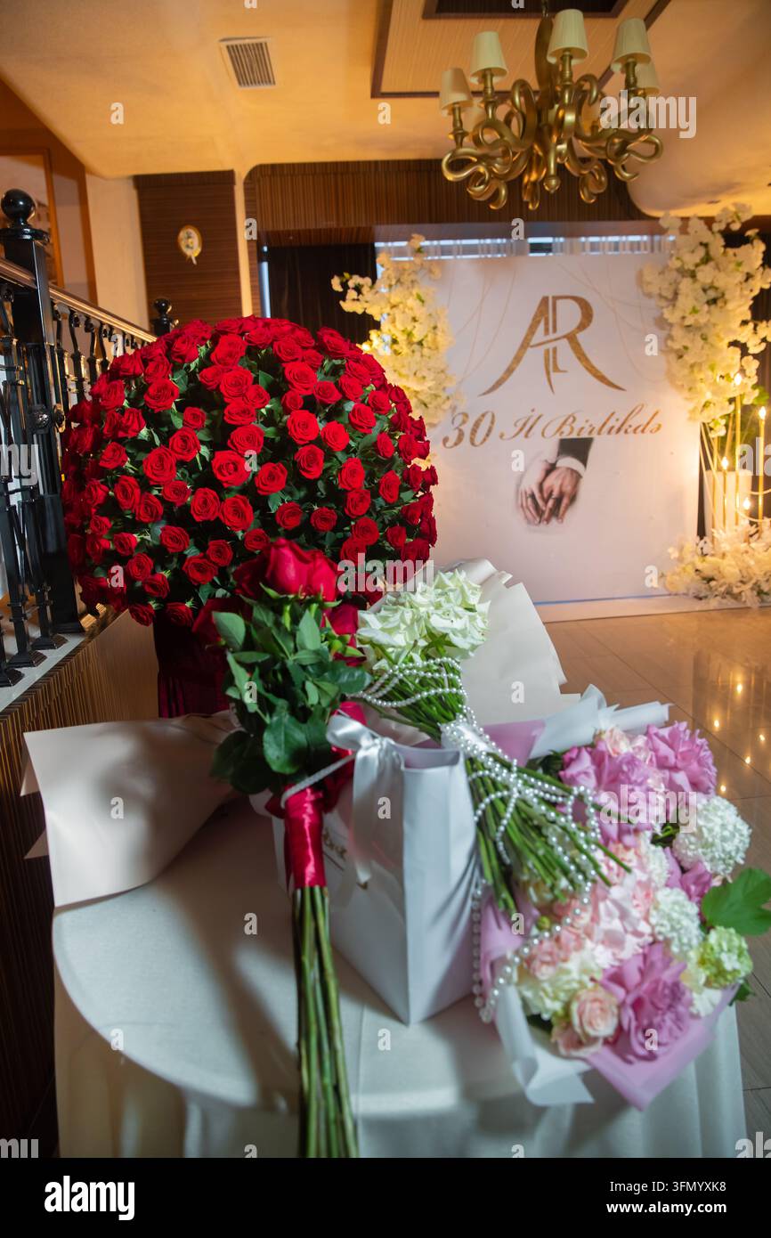 Décorations florales luxueuses placées sur une table devant une toile de fond personnalisée pour un événement. Magnifiques bouquets de fleurs et un immense arrangement de roses rouges Banque D'Images