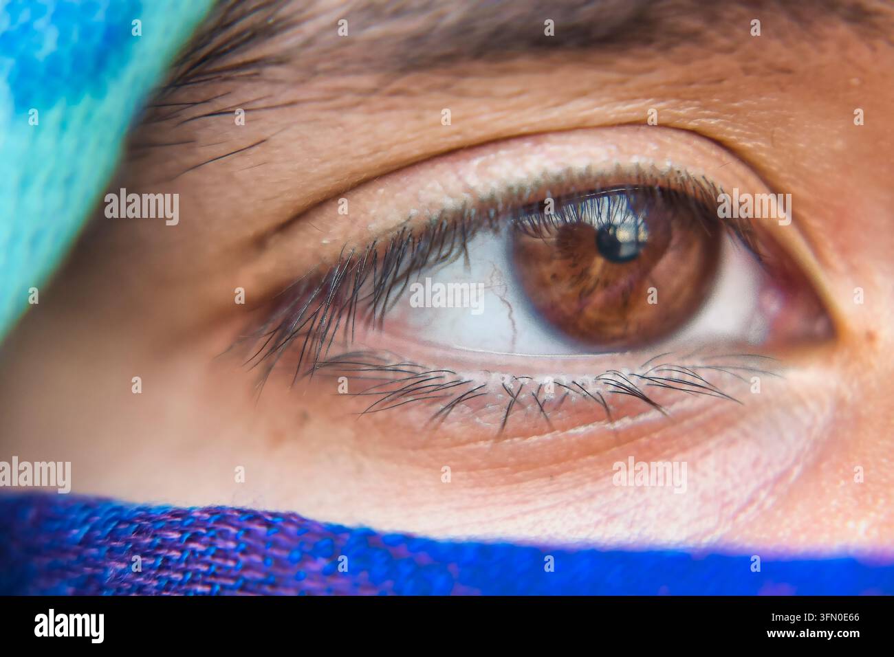 Œil marron de femme avec une iris et une pupille détaillées, regardant depuis derrière un foulard coloré Banque D'Images