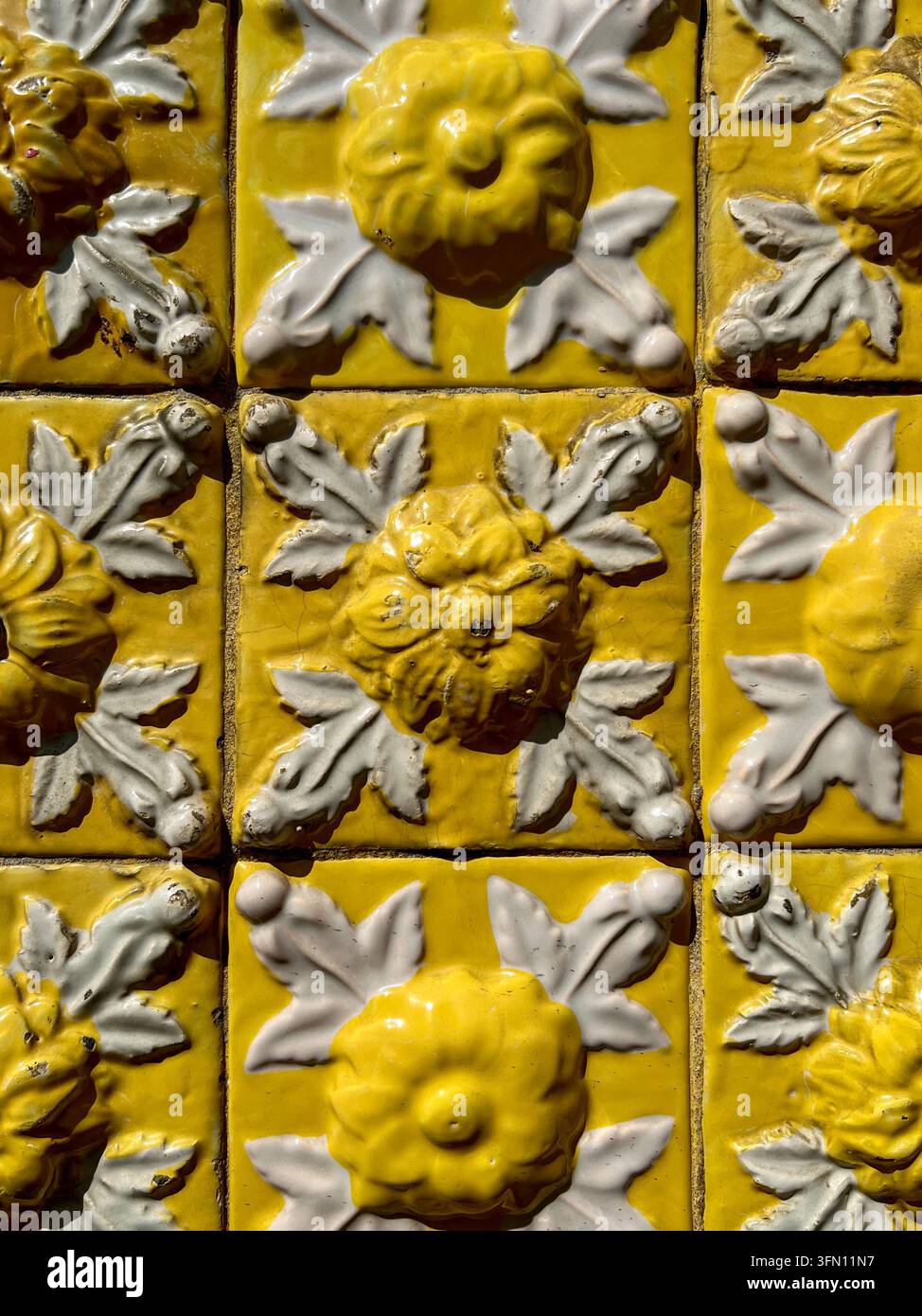 Carreaux azulejo jaunes et blancs en relief avec un motif floral en relief et une vernis brillant usé sur un mur au Portugal - Image de stock capturée avec un smartphone