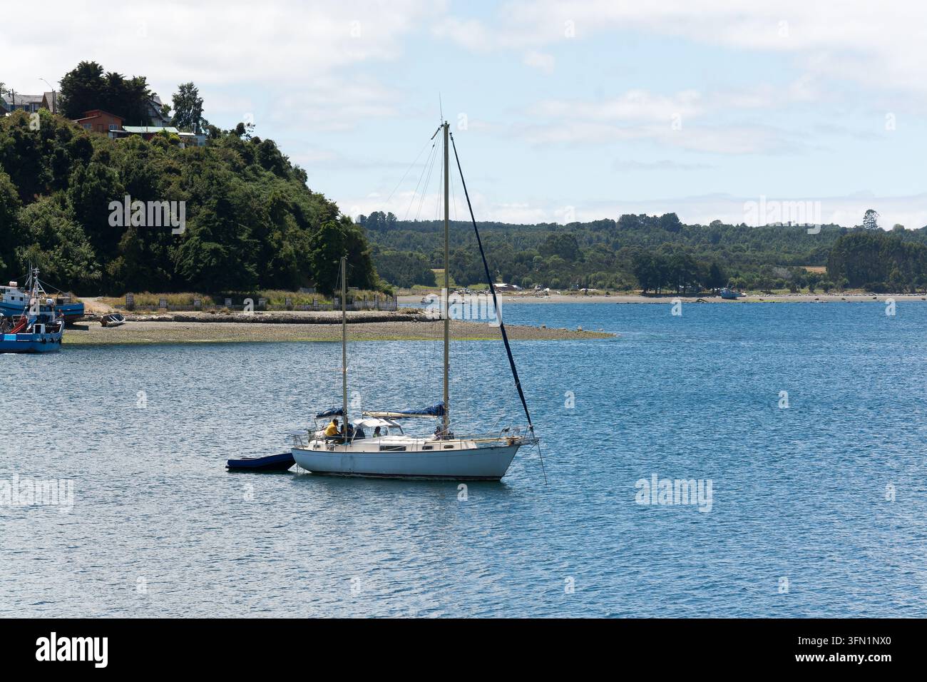 Yacht à voile blanc ancré près d'une colline côtière verte dans une baie marine bleue Banque D'Images