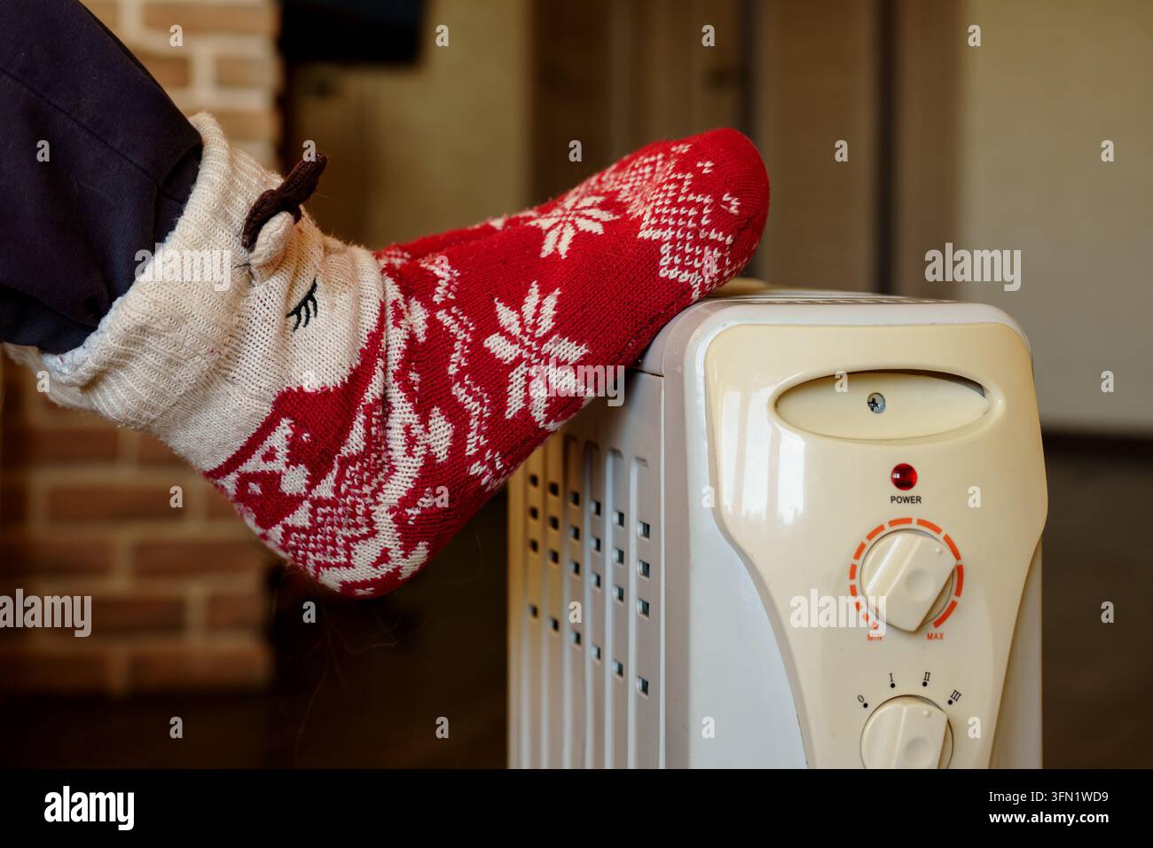 Jambes en chaussettes rouges se réchauffant près d'un radiateur électrique. Le concept de préparation hivernale et de confort saisonnier à la maison Banque D'Images