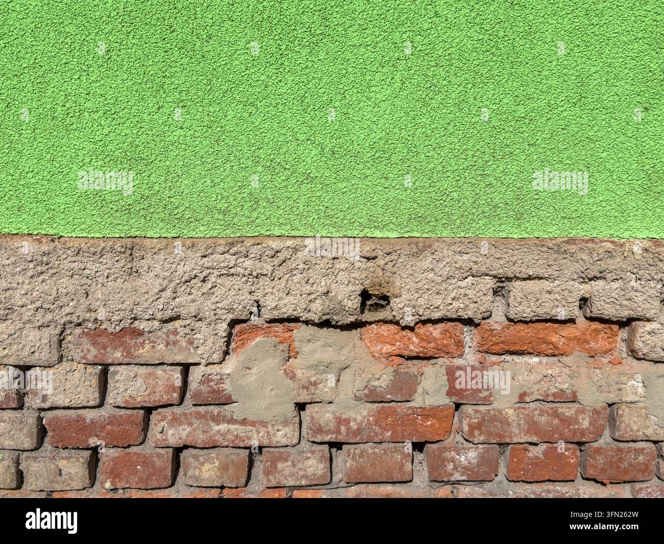 Un vieux mur de briques rouges partiellement recouvert d'un plâtre vert texturé, créant un contraste frappant entre la maçonnerie apparente et la surface usée. La a Banque D'Images