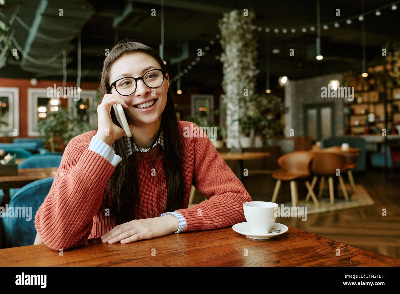 Femme heureuse parlant au smartphone assise dans un café avec un café Banque D'Images