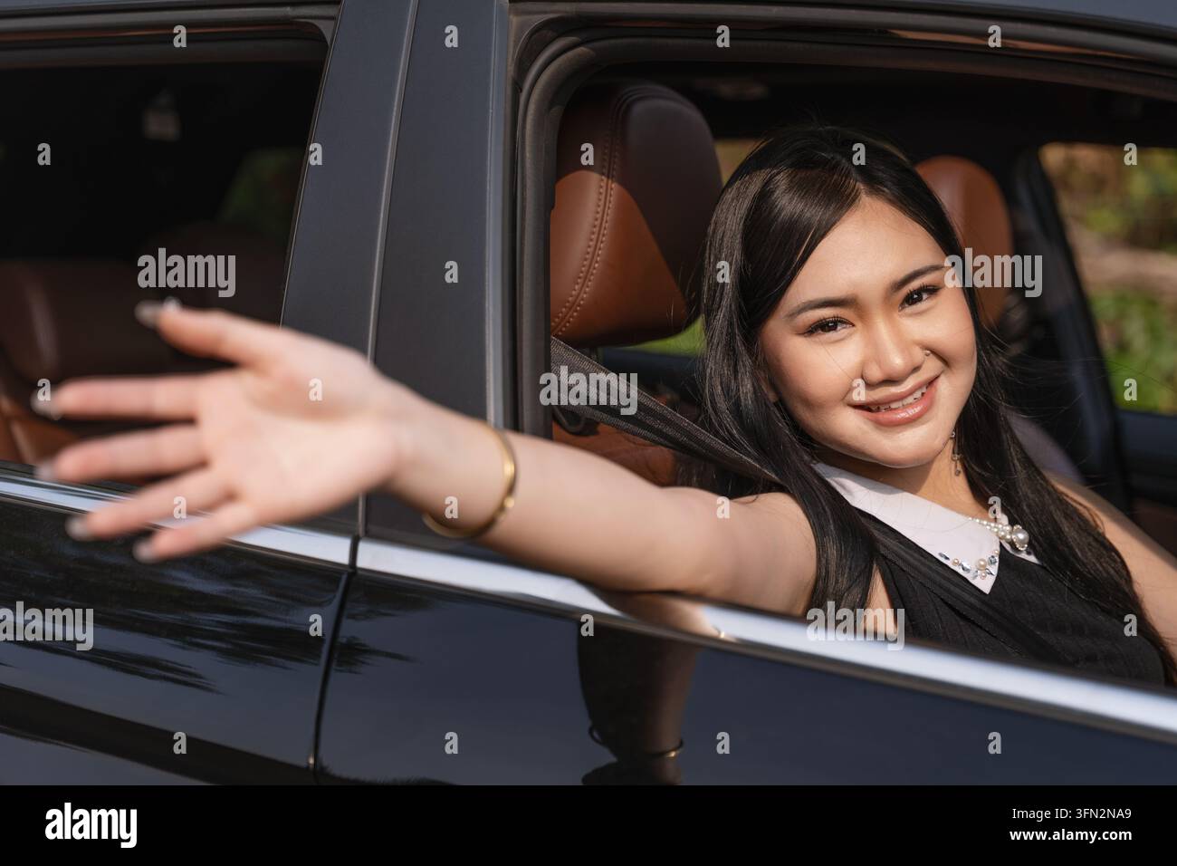 Jeune femme asiatique joyeuse souriant avec la main tendue par la fenêtre de la voiture. Banque D'Images