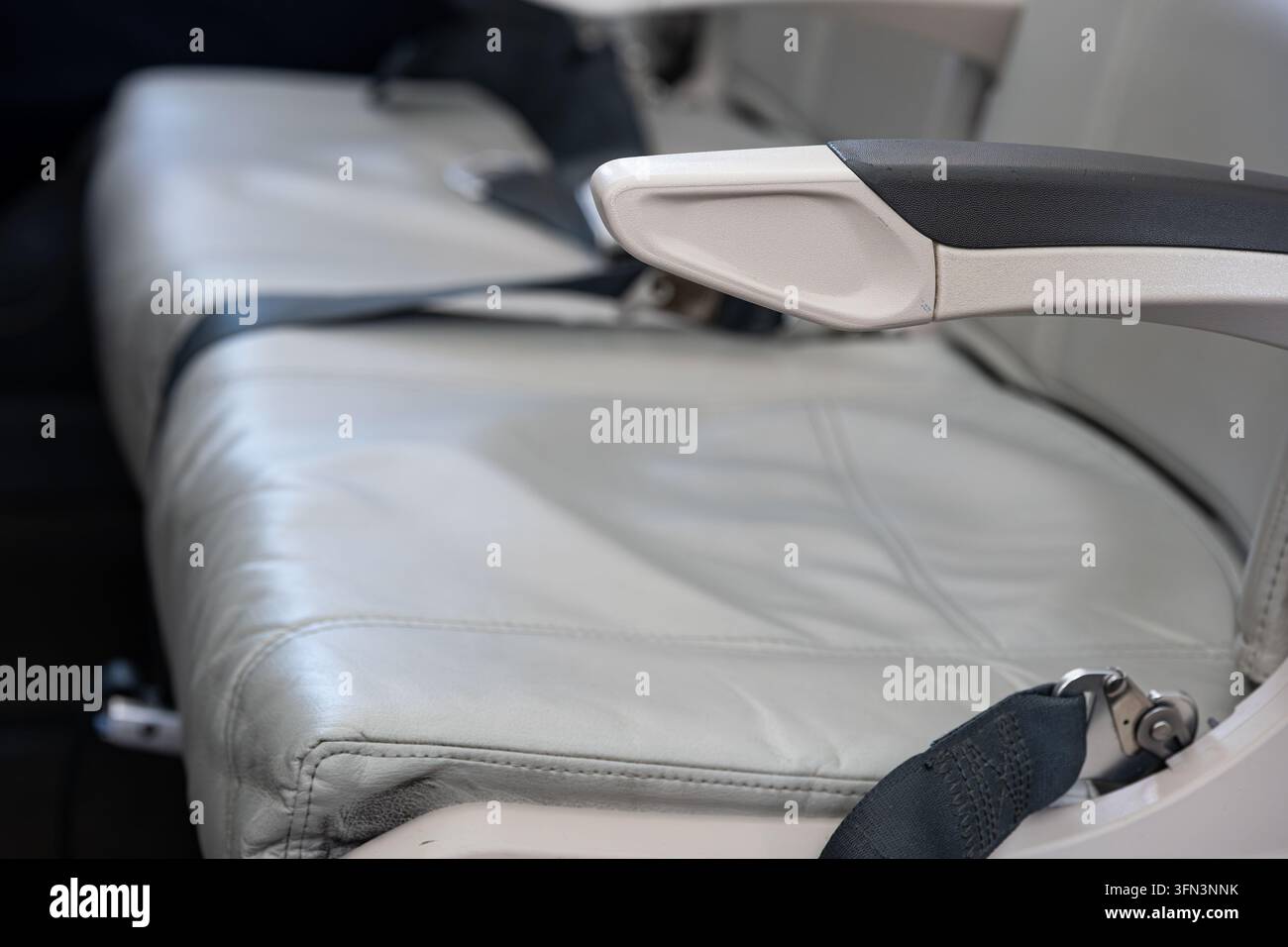 Vue détaillée montrant un siège passager en cuir gris vide, un accoudoir et une ceinture de sécurité à l'intérieur de la cabine d'un avion commercial pendant la préparation du vol Banque D'Images