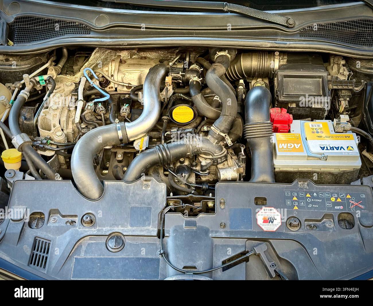 Vue avant du compartiment moteur ouvert d'une Renault Clio RS noire montrant le moteur turbocompressé, la batterie Varta AGM et l'emblème Renault Sport sur la calandre - Image de stock capturée avec un smartphone