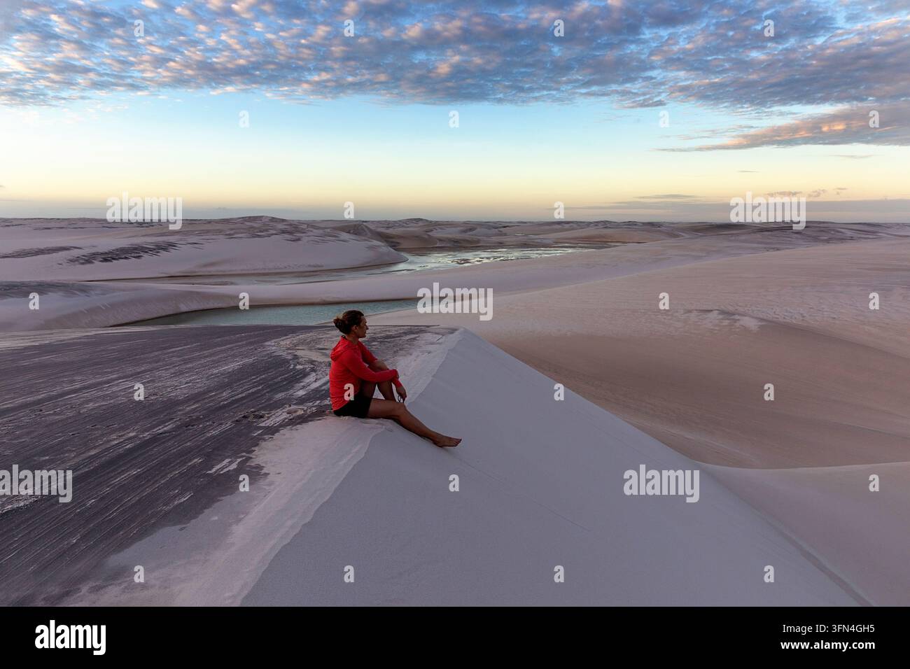 Une touriste féminine assise sur d'immenses dunes de sable blanc le soir, contemplant paisiblement le spectaculaire paysage des Lencois Maranhenses. Banque D'Images
