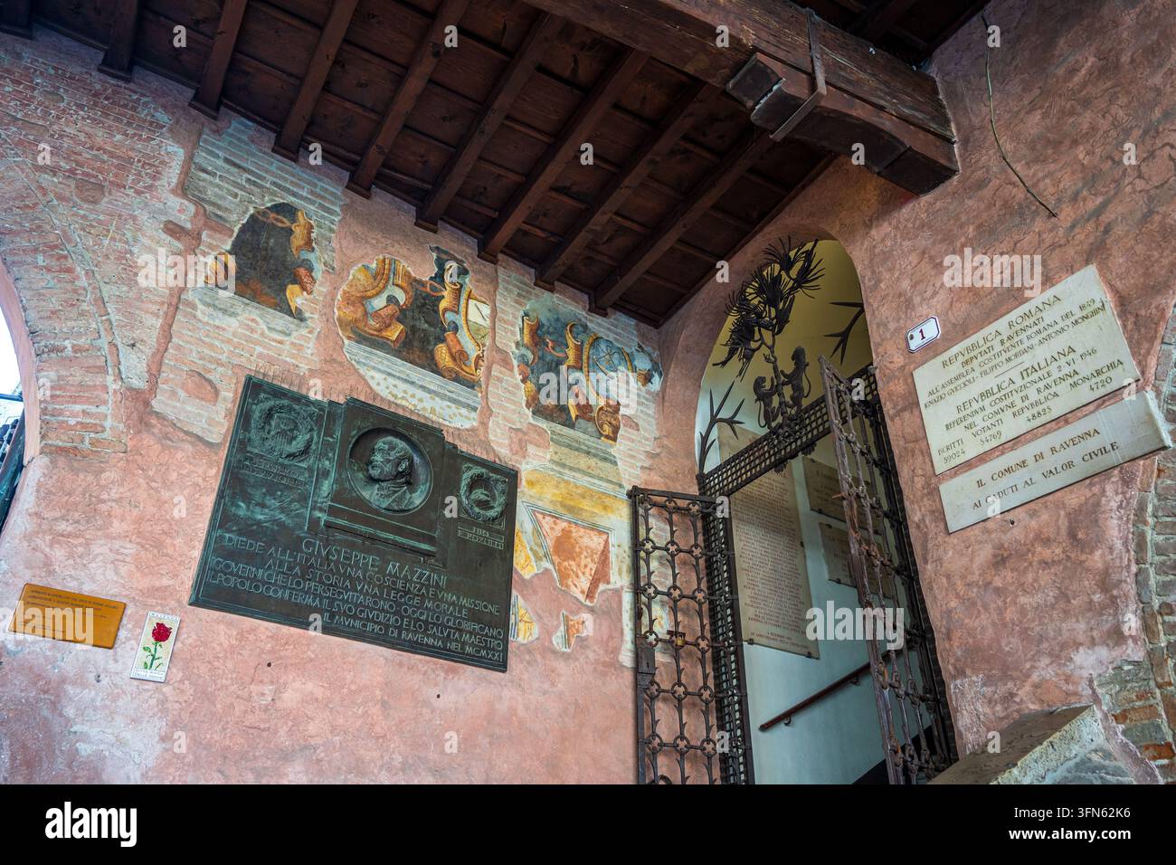 Détail intérieur de la mairie de Ravenne : plaque commémorative en bronze dédiée à Giuseppe Mazzini, entourée de fresques murales anciennes et colorées, laine sombre Banque D'Images