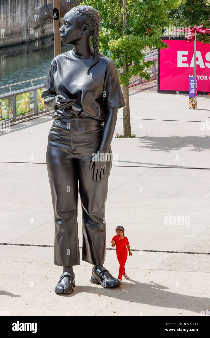 Sculpture Reaching Out par Thomas J Price à Stratford Londres avec une fille debout près de la figure noire Banque D'Images