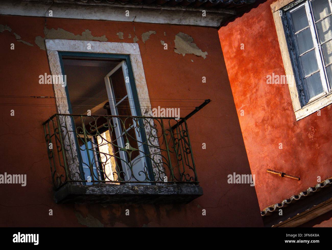 BALCON EN FER FORGE sur façade ocre rouge, contraste de lumière et d'ombre, maison de ville traditionnelle, cadre de fenêtre en pierre, Lisbonne, Portugal Banque D'Images
